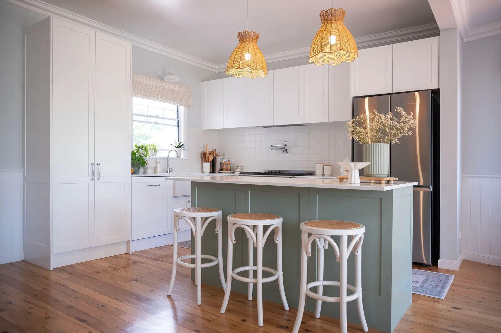 Modern kitchen with sage green island, white cabinetry and wicker pendant lights